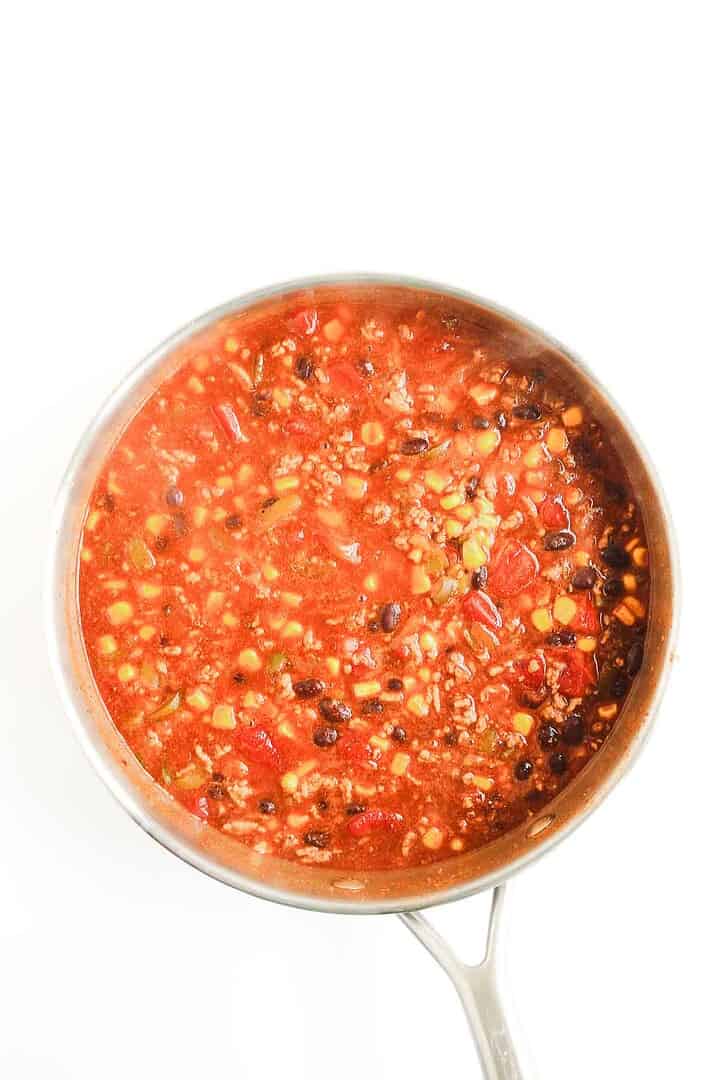 A pot of chili with ground meat, beans, tomatoes, and vegetables on a white background&mdash;perfect as inspiration for your next Beef Enchilada Casserole or favorite enchilada casserole recipe.