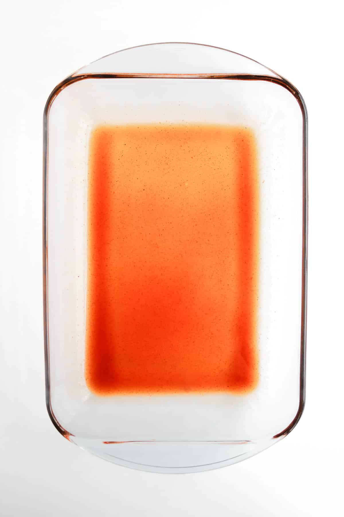 Rectangular glass dish with a small amount of reddish-orange liquid at the bottom, perfect for serving a Beef Enchilada Casserole, on a white background.