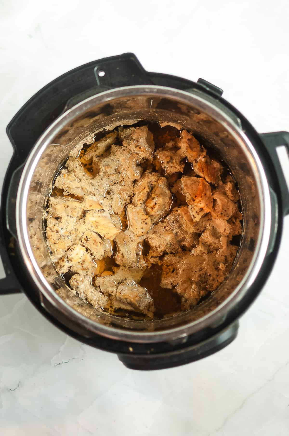 An Instant Pot filled with tender, browned carnitas and savory juices on a light countertop.