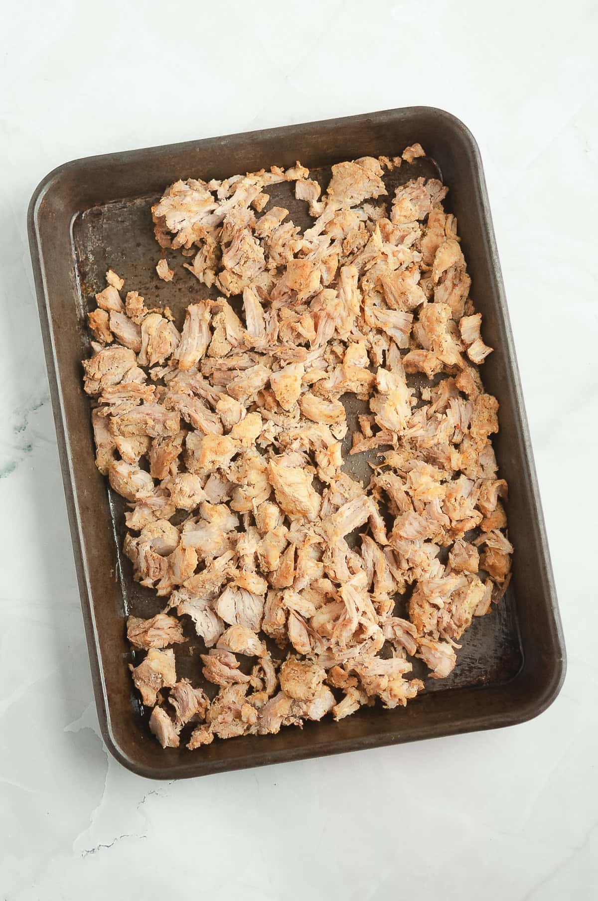 Shredded cooked chicken, prepared in the Instant Pot, is spread evenly on a rectangular baking tray over a white marble surface.