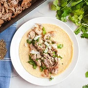 A tortilla topped with savory Instant Pot Carnitas, chopped onions, and cilantro on a white plate beside fresh cilantro—a delicious twist on the classic Carnitas recipe.