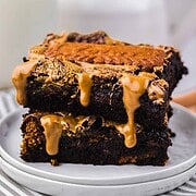 Two chocolate brownies stacked, topped with a drizzle of melted peanut butter, on a white plate—a tempting Biscoff Brownie treat.