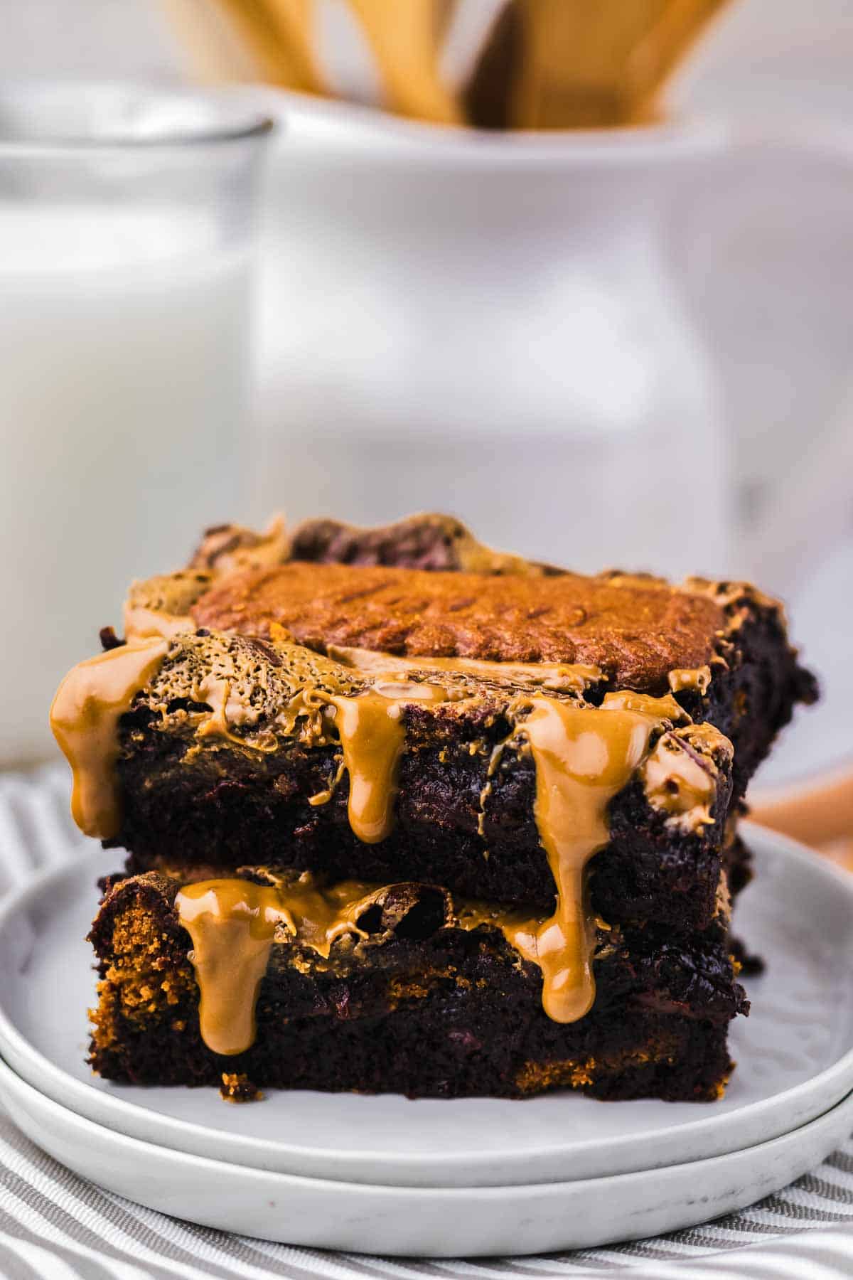 Two chocolate brownies stacked, topped with a drizzle of melted peanut butter, on a white plate—a tempting Biscoff Brownie treat.