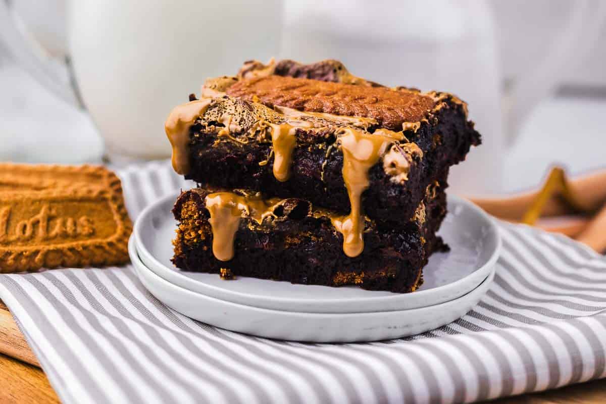 Two indulgent Biscoff Brownies topped with melted cookie butter, stacked on a plate and served with a Lotus biscuit on the side—a must-try for any brownie recipe lover.