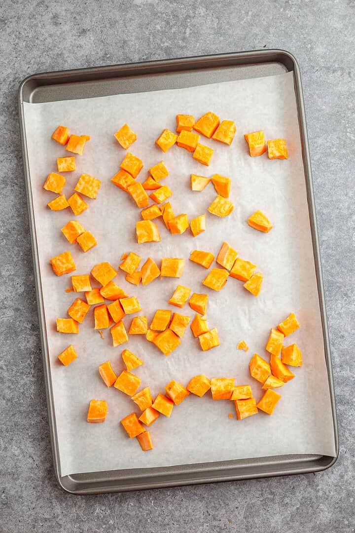 Diced orange sweet potatoes and sausage spread out on a parchment-lined sheet pan.