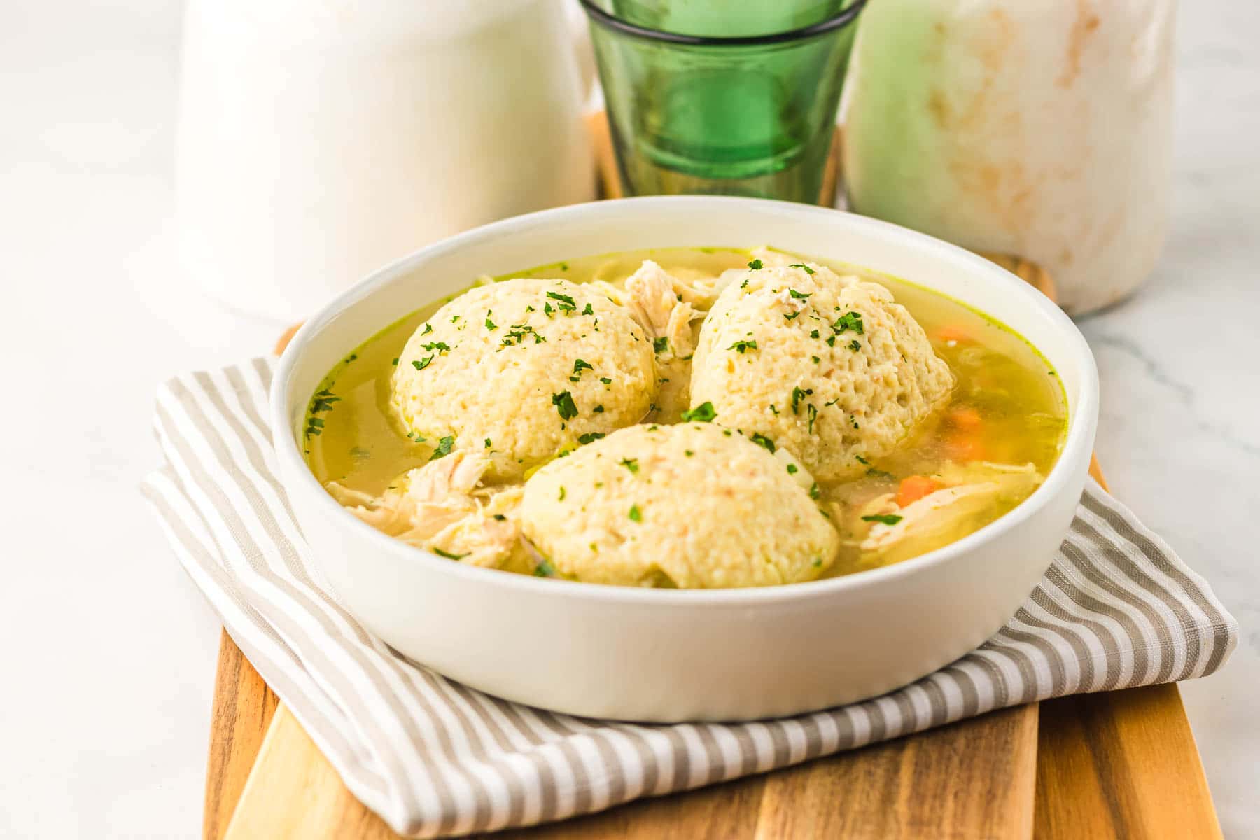 A bowl of chicken and dumplings soup with three dumplings, served on a striped napkin—a comforting recipe reminiscent of classic Matzo Ball Soup.