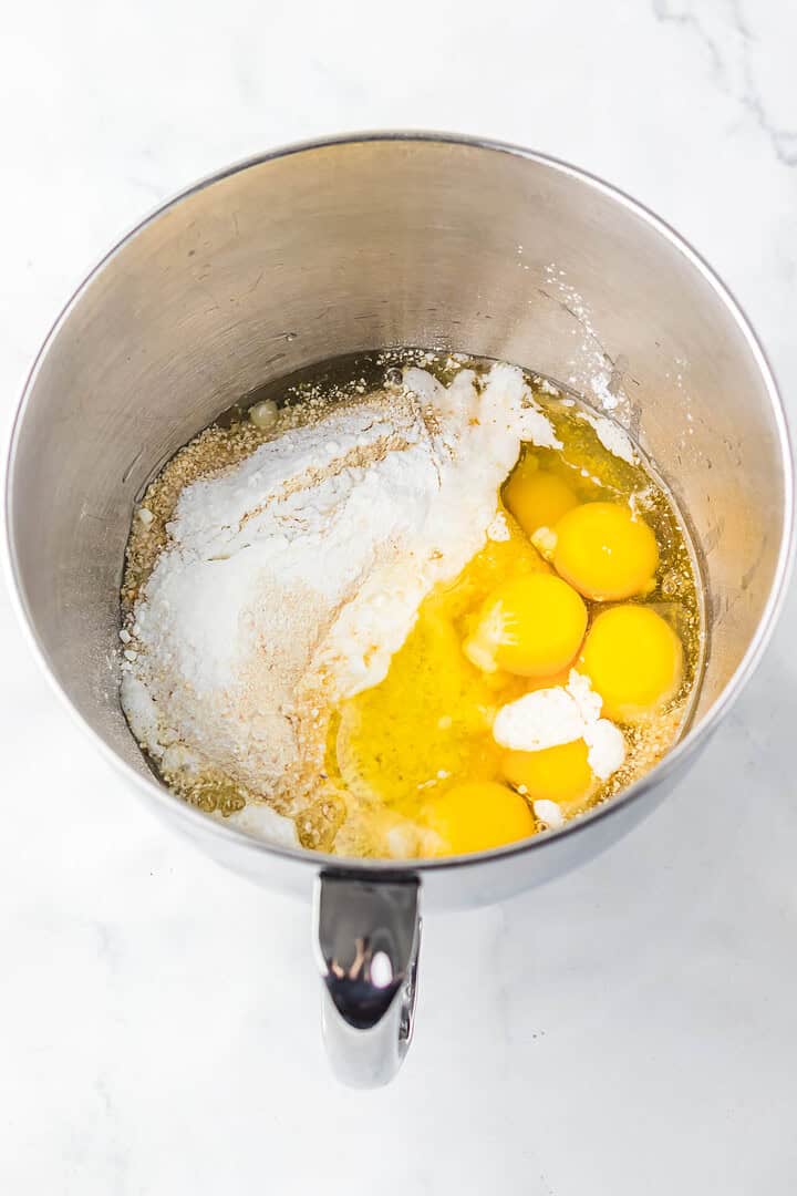 A mixing bowl with eggs, flour, sugar, and other baking ingredients on a white countertop—perfect for prepping a new recipe or adding to your favorite Matzo Ball Soup tradition.
