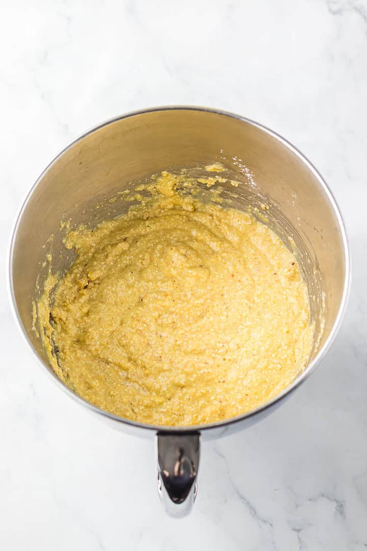 Yellow grainy batter in a stainless steel mixing bowl on a white marble surface, ready to be transformed into matzo balls for a classic Matzo Ball Soup recipe.