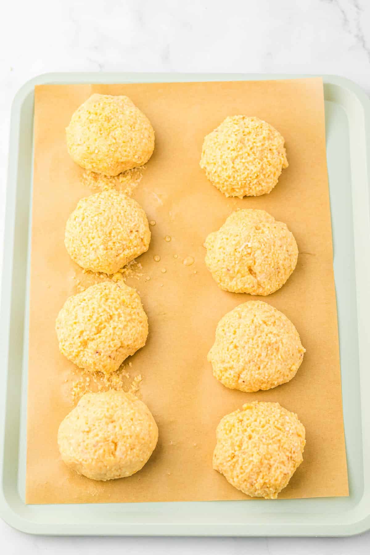 Eight unbaked biscuit dough balls on a parchment-lined baking sheet, ready to go in the oven—perfect for pairing with your favorite slow cooker recipe or a warm bowl of matzo ball soup.