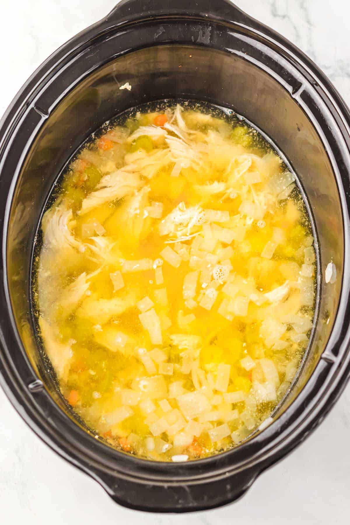 A comforting recipe for chicken soup with shredded chicken, diced onions, and vegetables in a slow cooker with savory broth—perfect for those who love classic flavors or a twist like matzo ball soup.