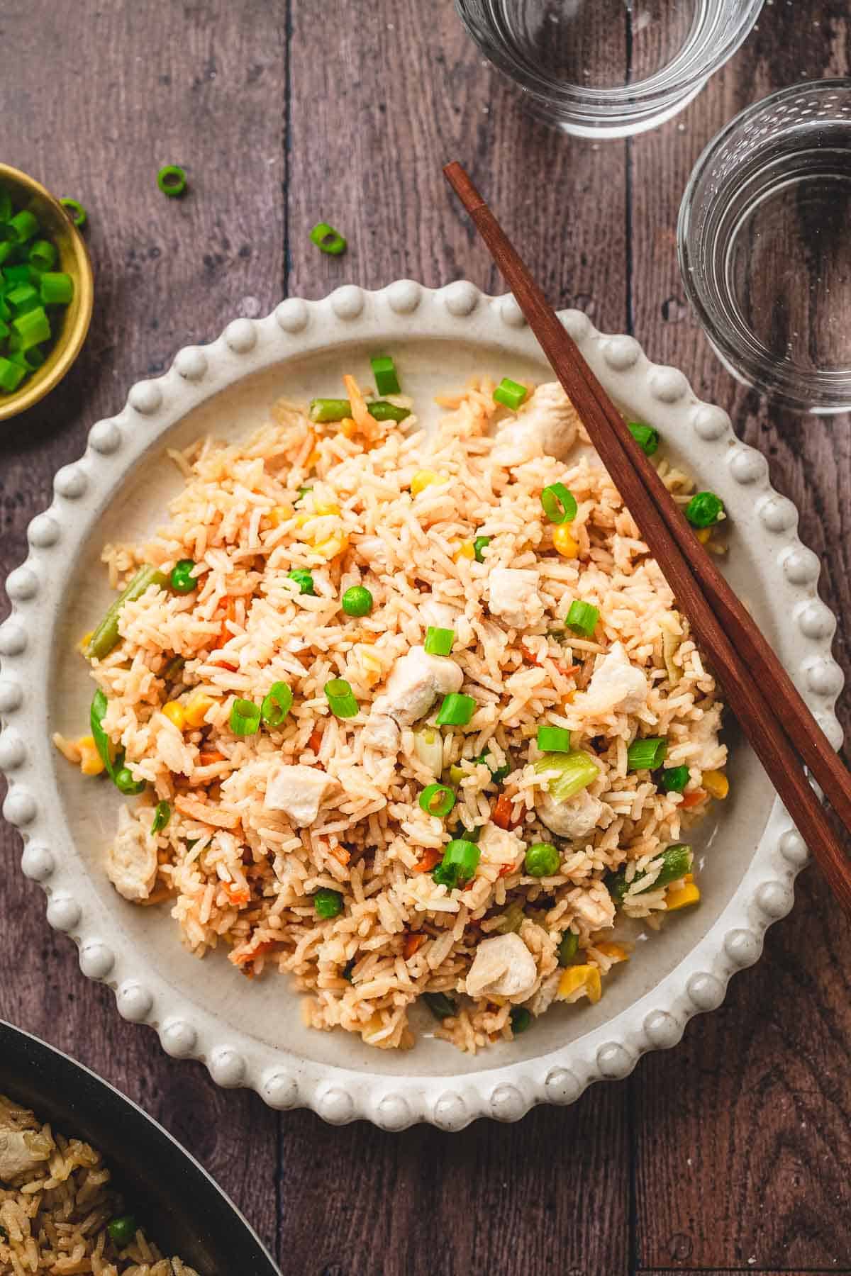 A plate of crispy fried rice garnished with green onions, served with chopsticks on a wooden table&mdash;a classic recipe perfect for any meal.
