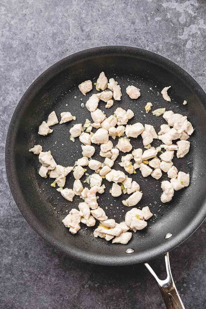 Small pieces of chicken sizzle in a black frying pan on a gray countertop, perfect for a teriyaki chicken recipe.