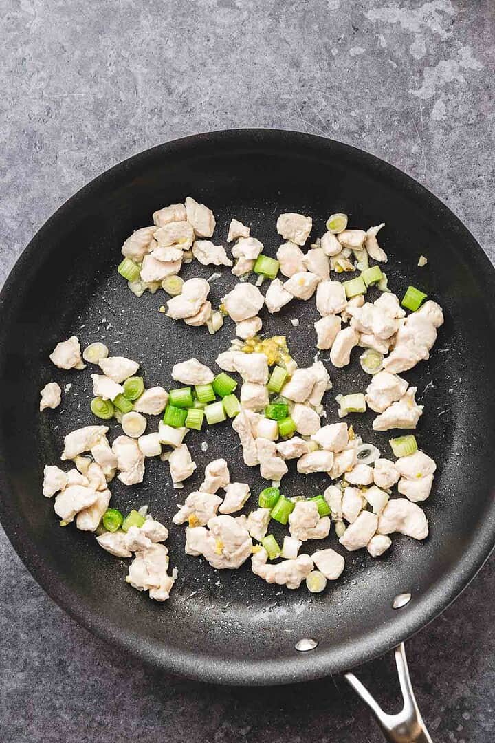 Chopped teriyaki chicken and green onions sizzle in a black skillet on a gray countertop&mdash;perfect for your next fried rice recipe.