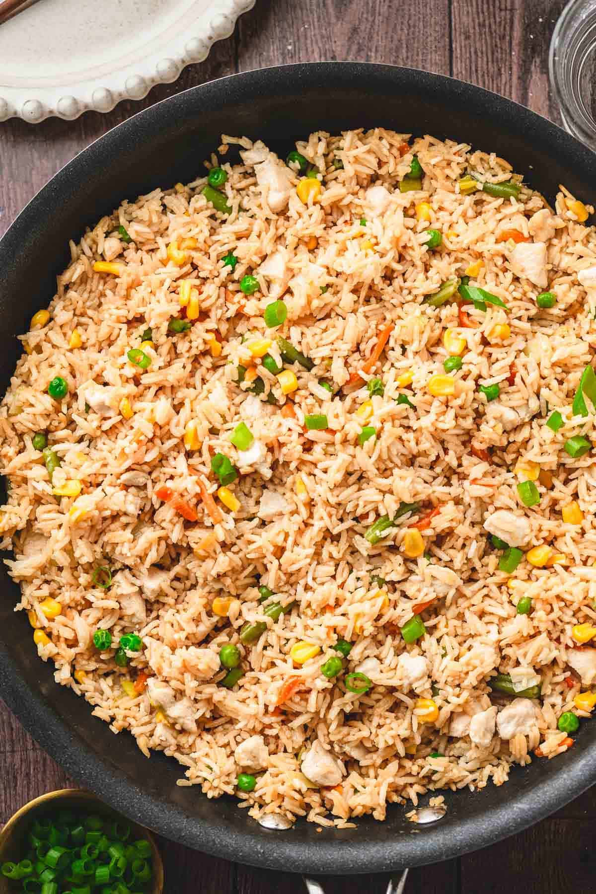 A skillet filled with flavorful fried rice, mixed with peas, corn, carrots, and chopped green onions&mdash;an easy recipe perfect alongside teriyaki chicken.