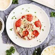 Enjoy these Homemade Pizza Bagels topped with melted cheese, zesty pepperoni, and fresh herbs, served on a white plate with a parsley garnish.
