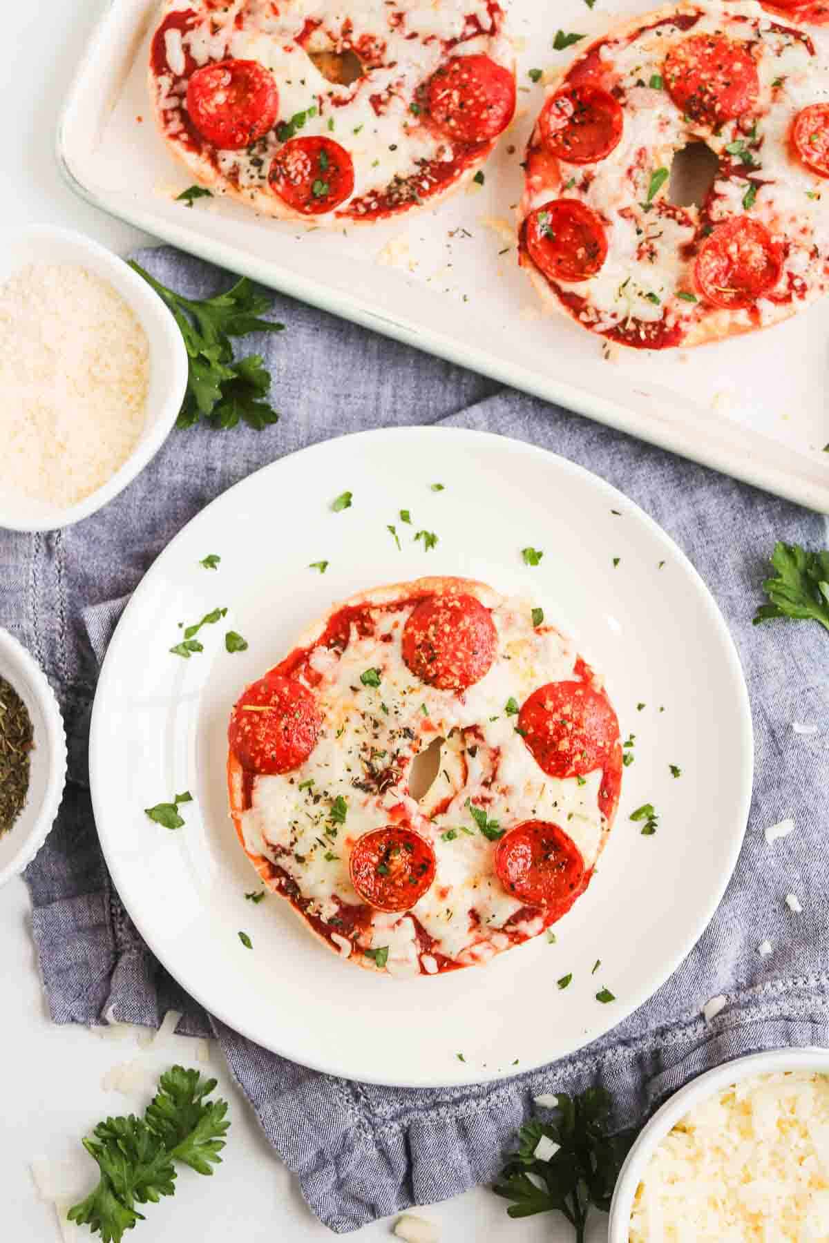 Enjoy these Homemade Pizza Bagels topped with melted cheese, zesty pepperoni, and fresh herbs, served on a white plate with a parsley garnish.