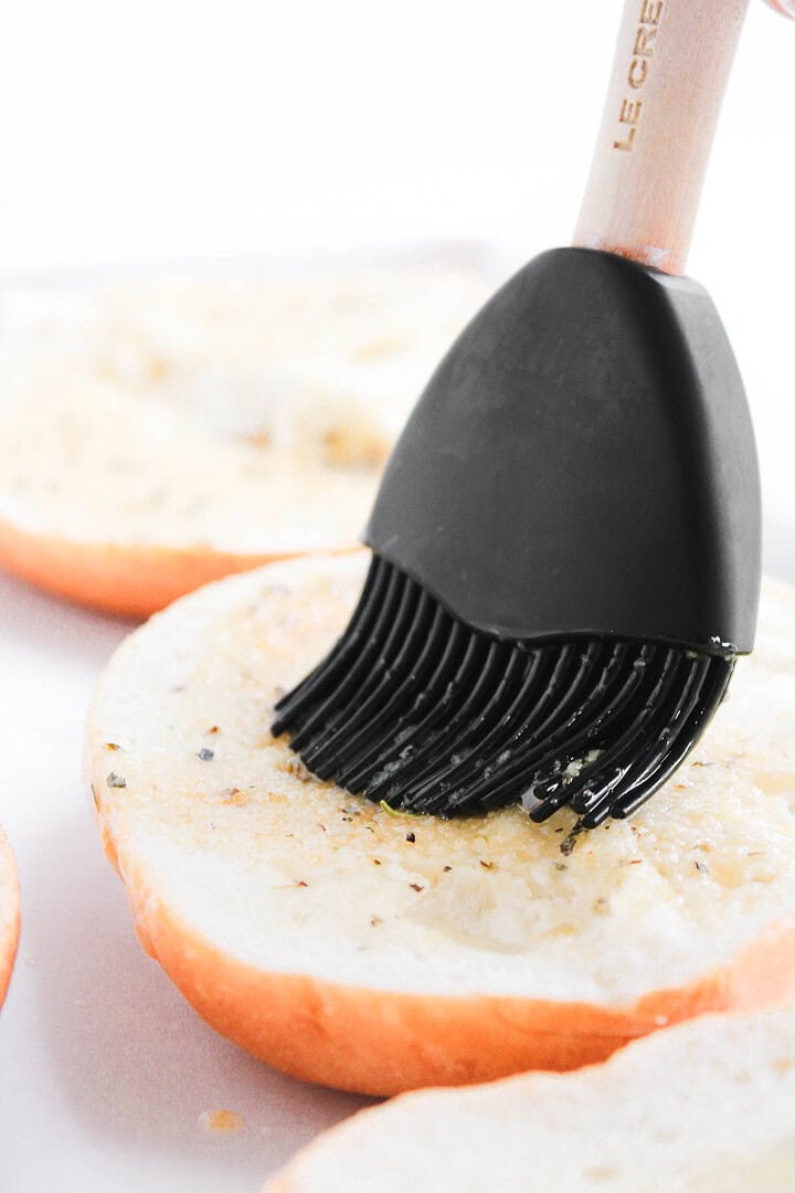 A silicone brush spreading seasoning and oil on a sliced piece of homemade bread.
