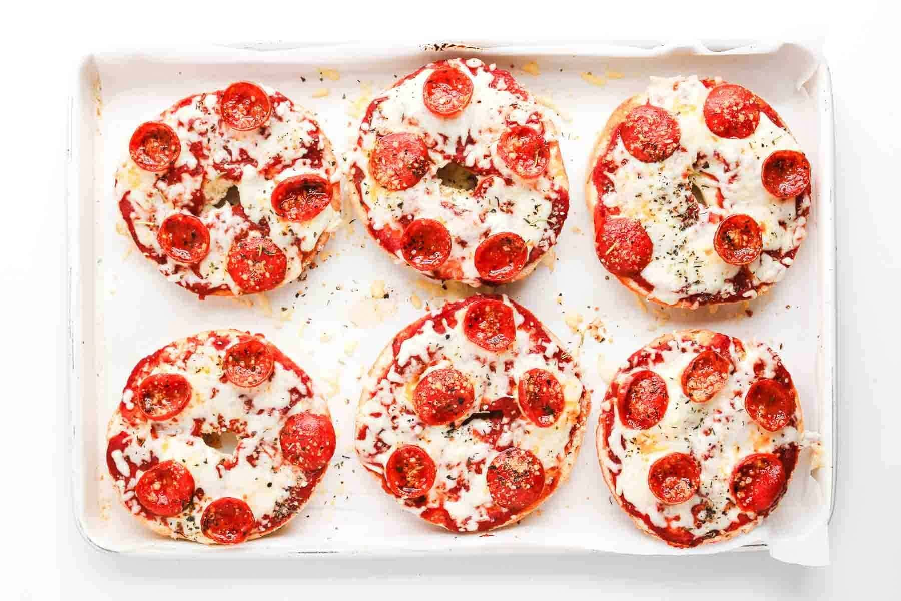 Six mini Pepperoni Pizza Bagels with melted cheese on a baking sheet, viewed from above.