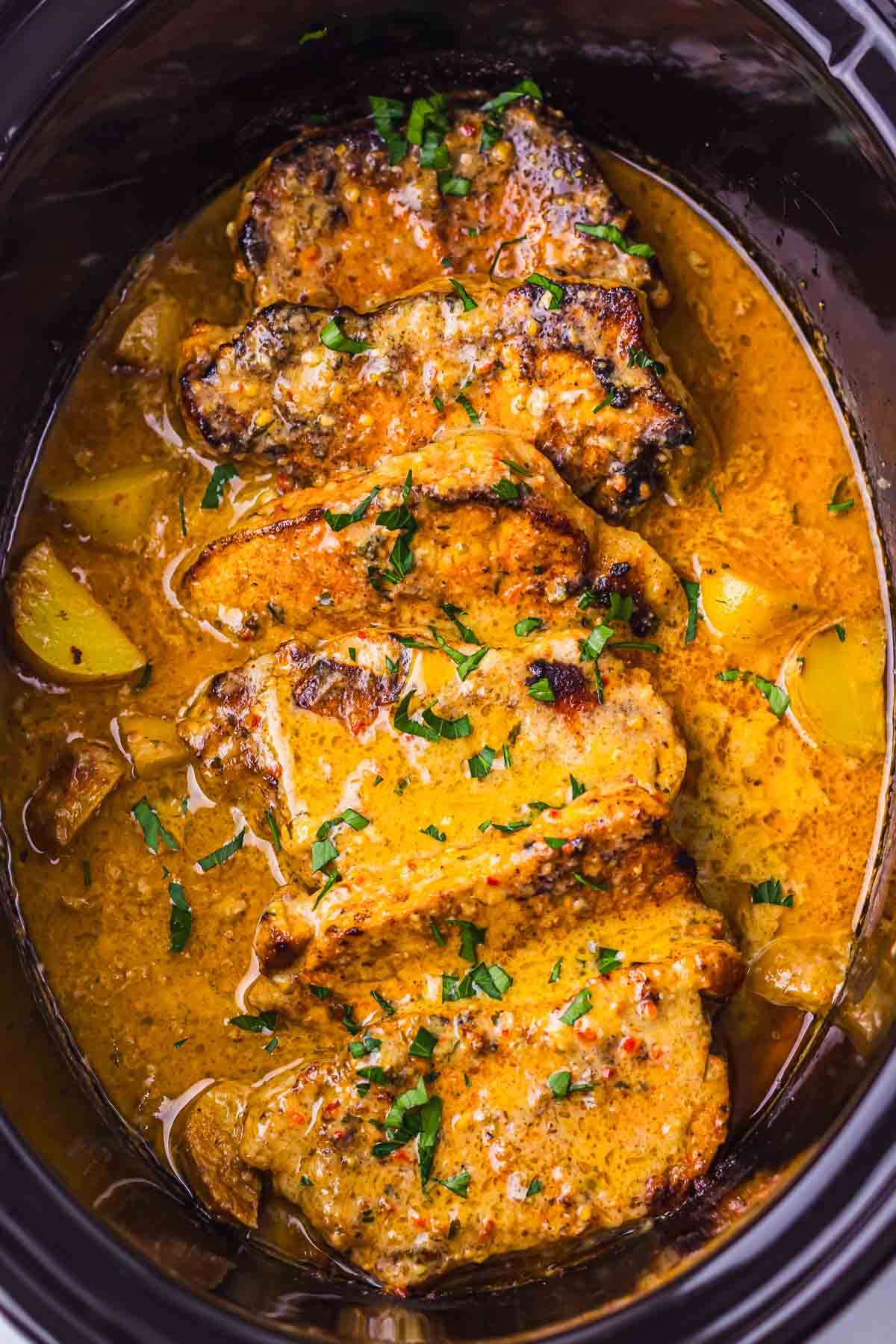 Enjoy garlic parmesan pork chops in a creamy herb sauce with tender potatoes, all made effortlessly in your slow cooker for a comforting meal.