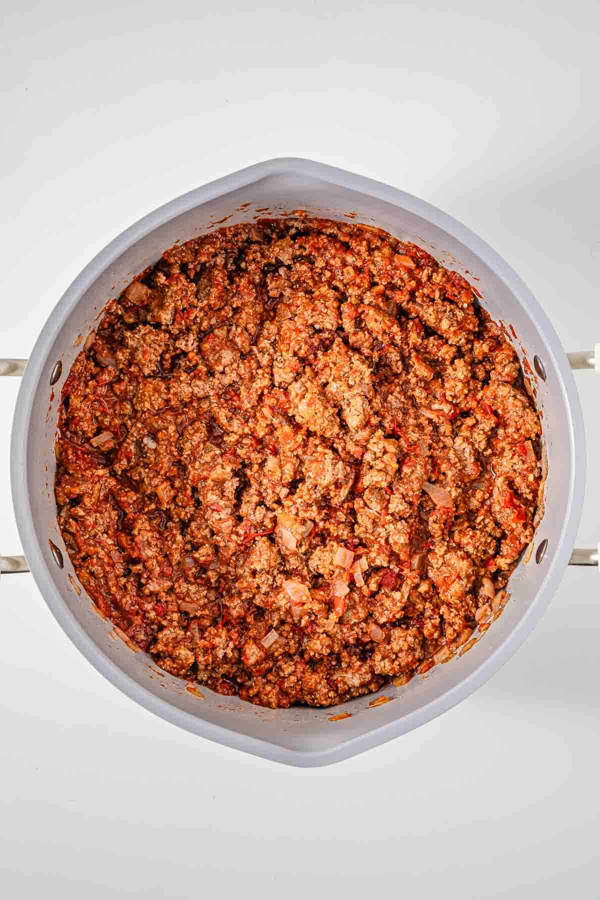 A pan filled with cooked ground meat mixed with tomato sauce and diced onions, seen from above&mdash;perfect as an easy chili or a flavorful hot dog chili for your next meal.