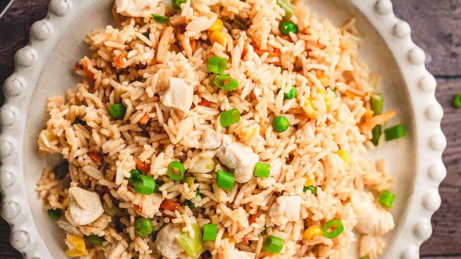 A plate of fried rice with vegetables, chicken pieces, and chopped green onions, with chopsticks on the side.