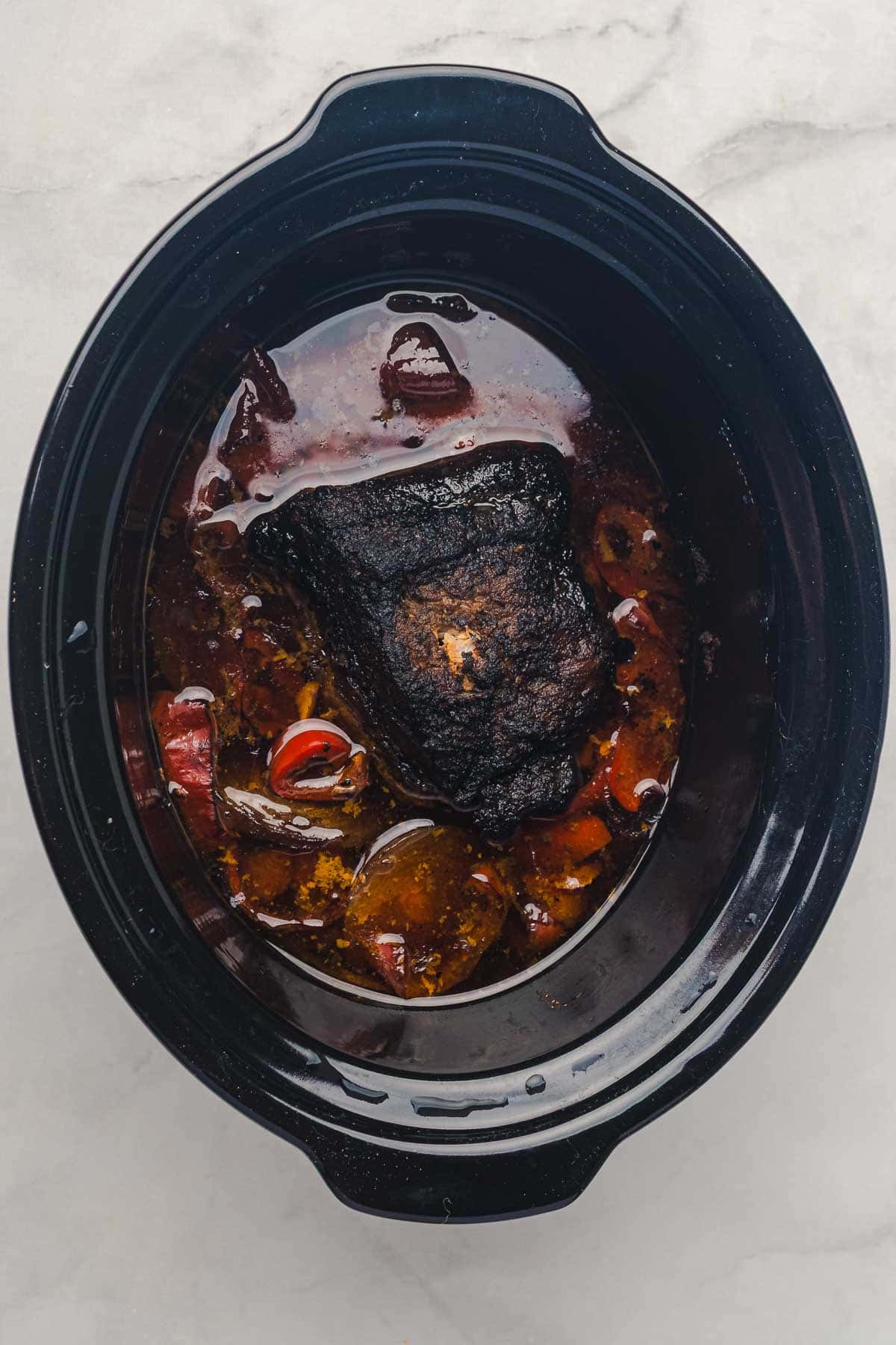 A flavorful slow cooker Tex Mex pulled pork with vegetables and savory broth, served in a black slow cooker on a marble countertop.