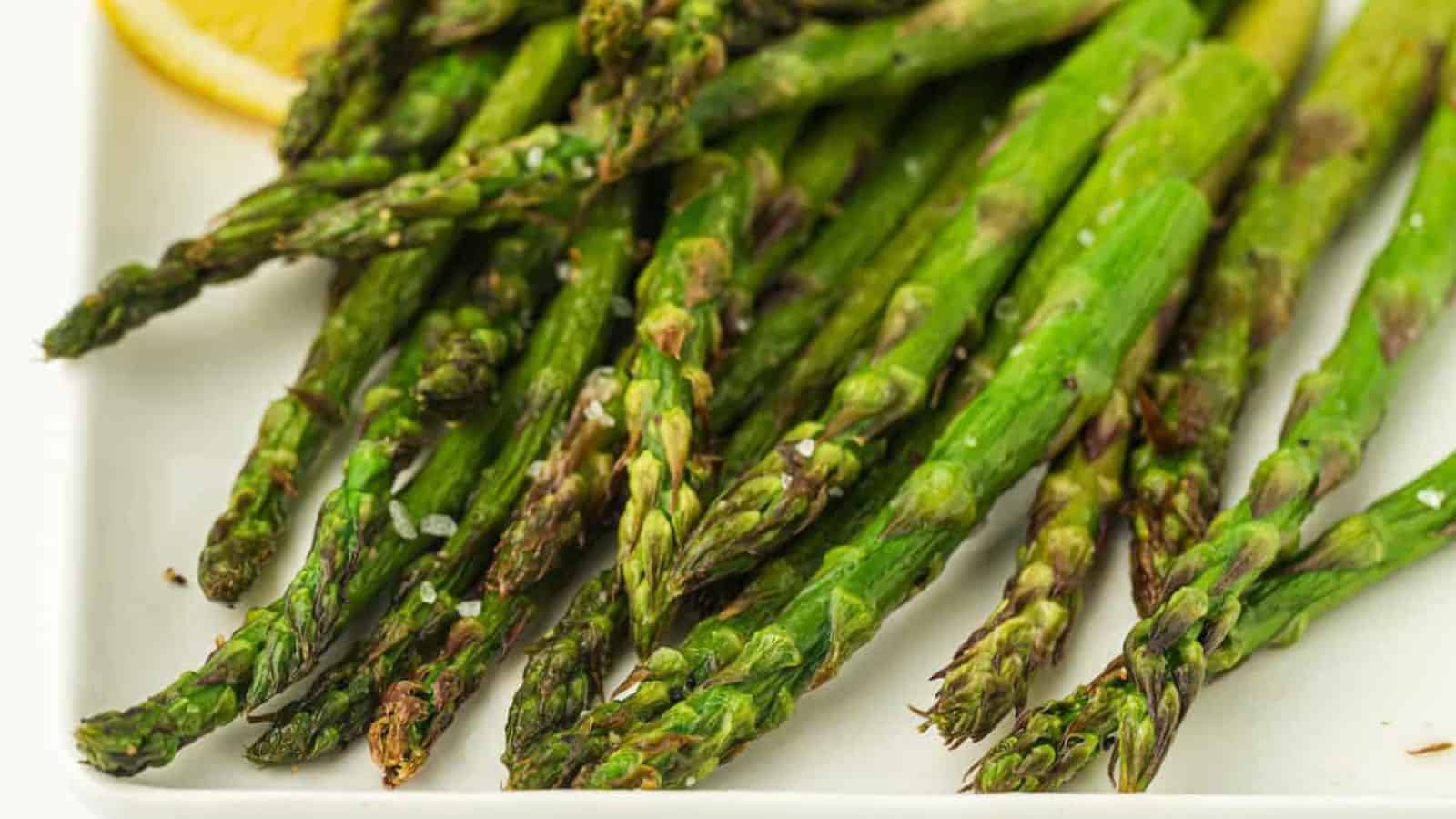 A plate of cooked asparagus spears garnished with sea salt and a lemon wedge.