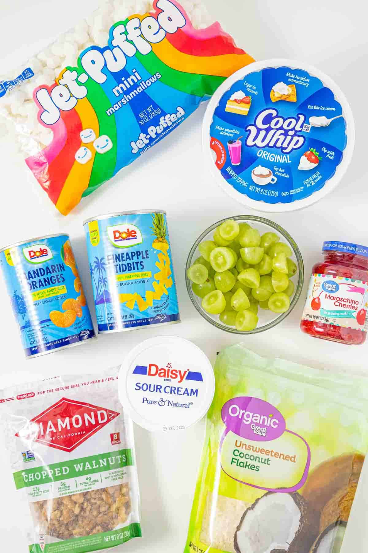 Assorted ingredients for a dessert, including marshmallows, Cool Whip, fruit, sour cream, nuts, and coconut flakes&mdash;everything you need for a classic Ambrosia or Fluff Salad recipe.