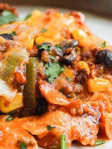 Close-up of a cheesy, baked casserole with corn, beans, and ground meat, garnished with chopped herbs.