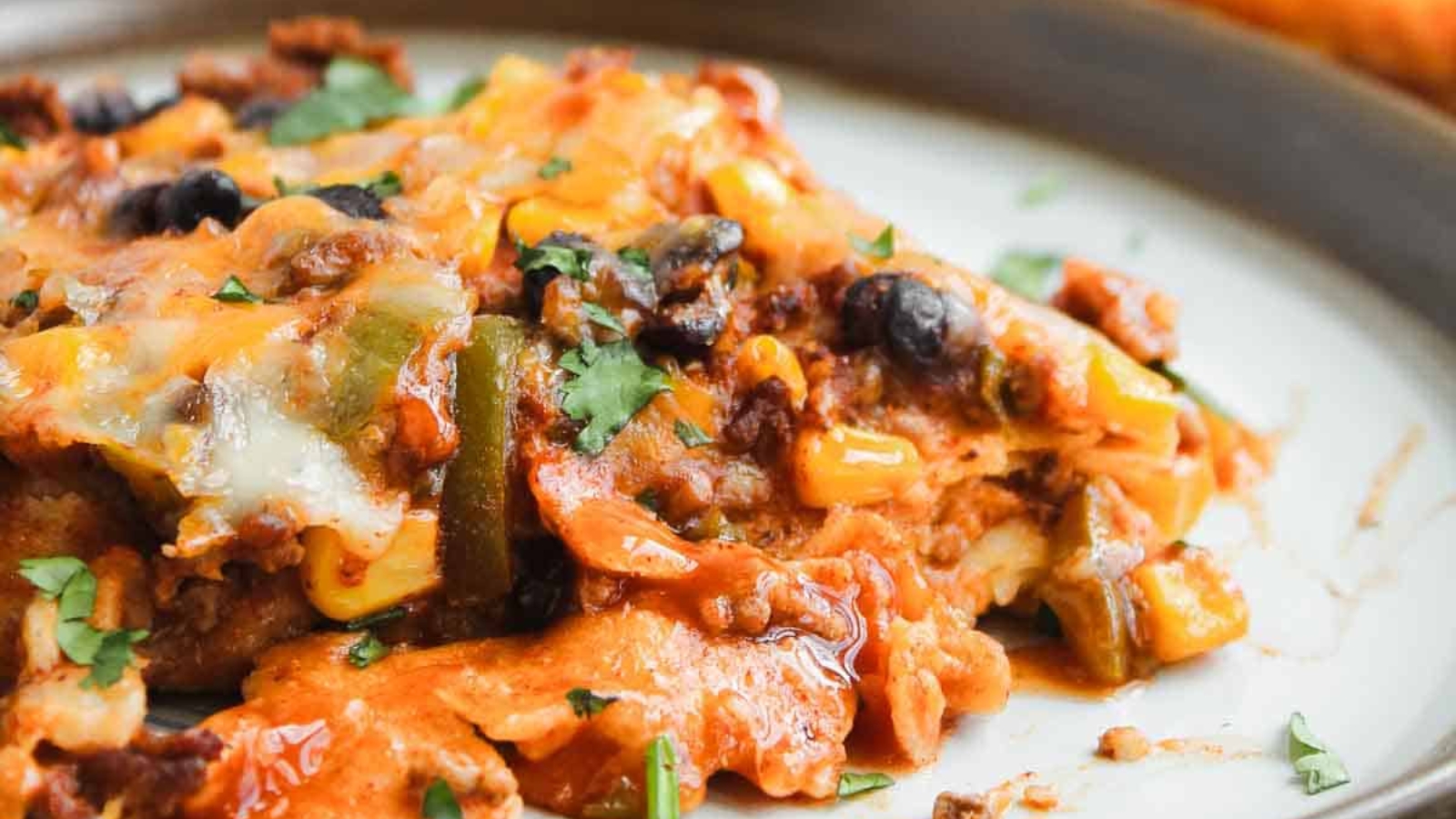 A casserole topped with melted cheese, black beans, corn, sour cream, lime slices, and cilantro in a glass dish.