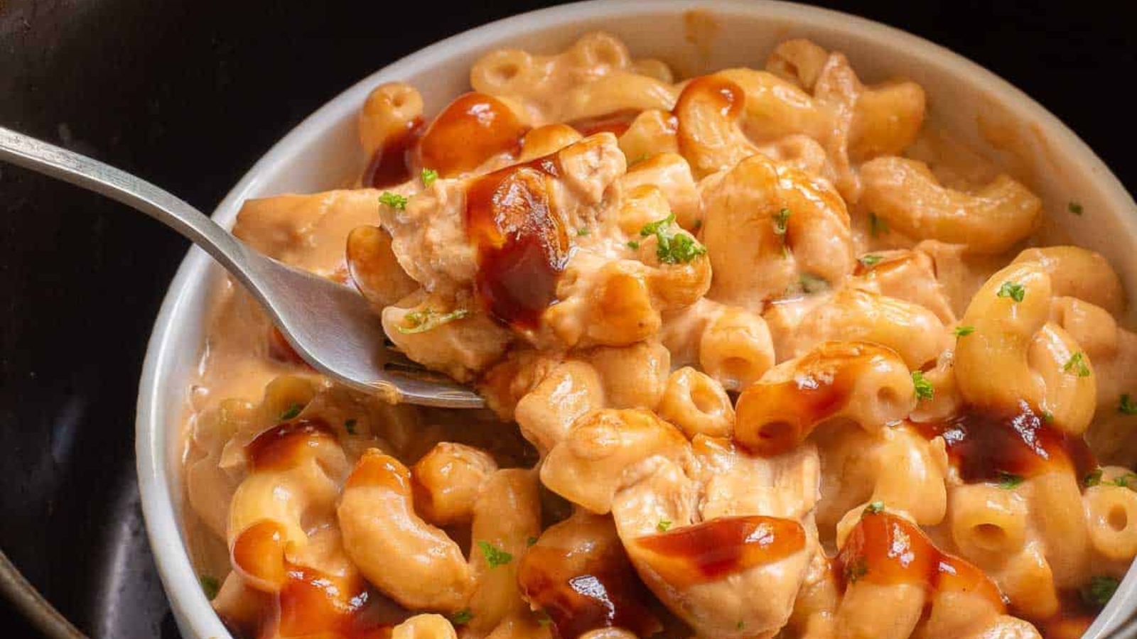 Bowl of creamy macaroni and cheese with chicken and barbecue sauce, topped with chopped herbs&mdash;a delicious twist on classic comfort using air fryer recipes.