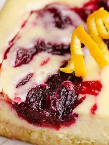 A cheesecake bar with berry swirl and orange zest topping on a white plate with a fork—perfect for budget Mother’s Day desserts.