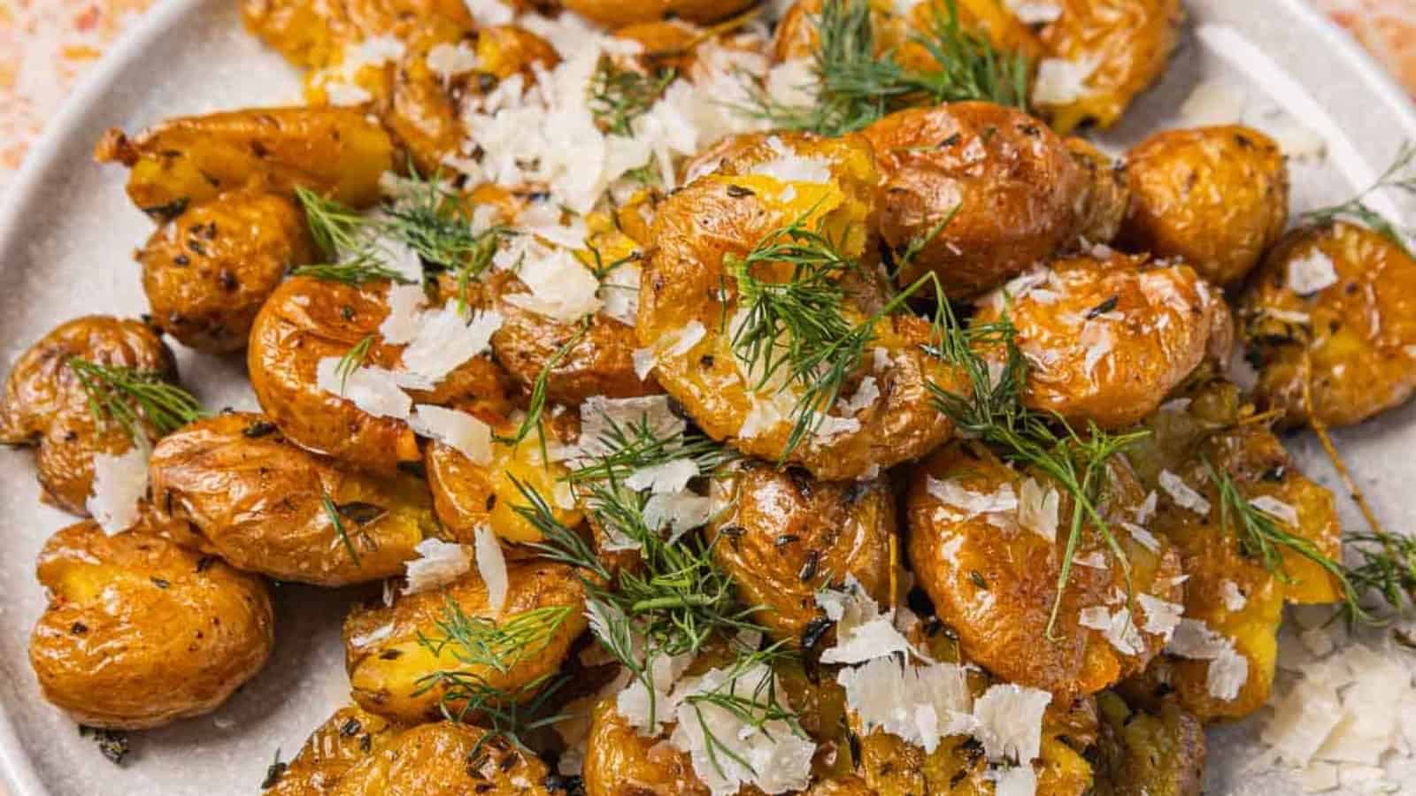 Crispy smashed potatoes topped with fresh dill and shredded Parmesan cheese on a plate.