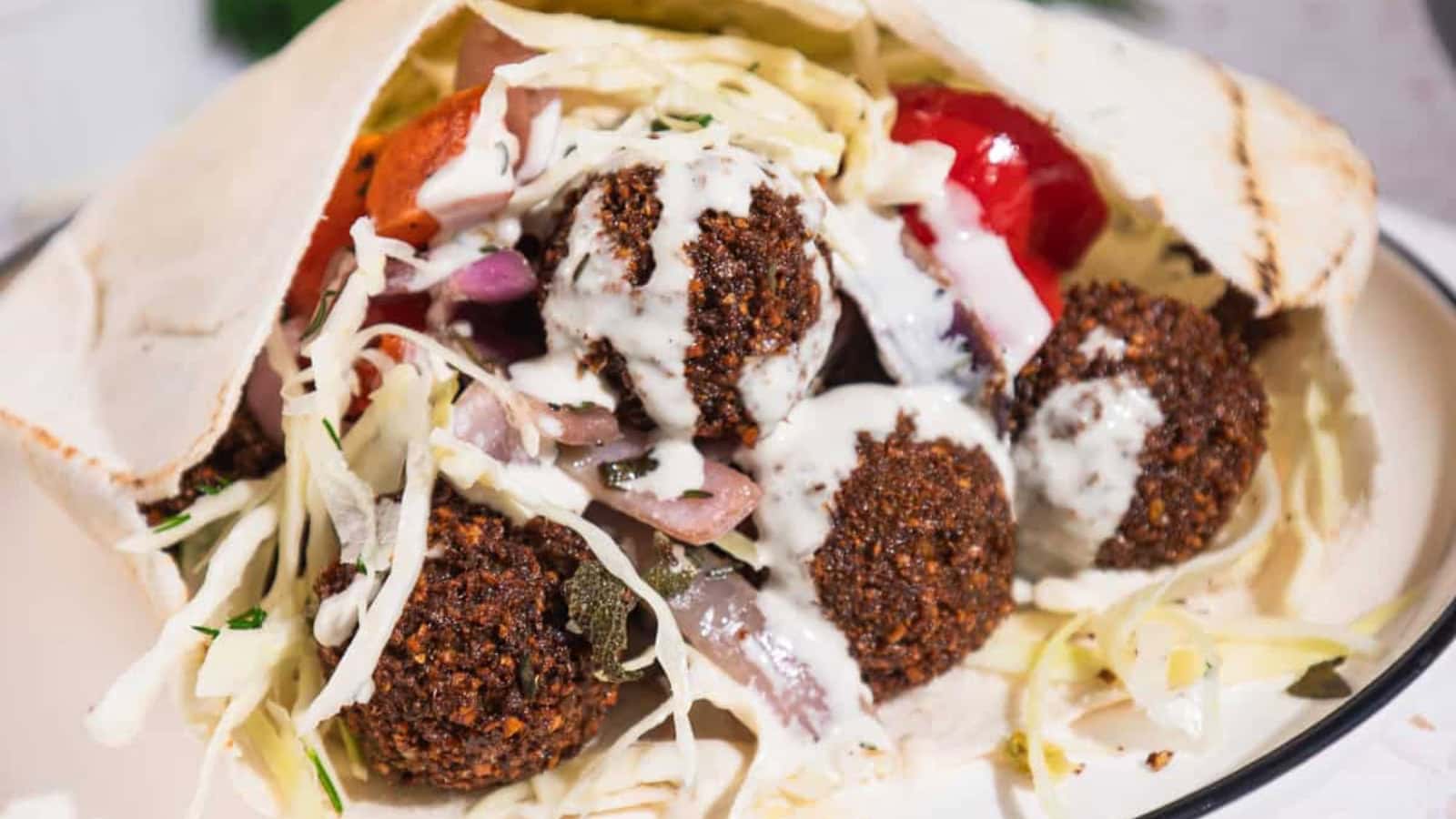 Close-up of a pita filled with falafel, shredded cabbage, tomatoes, onions, and drizzled with white sauce.