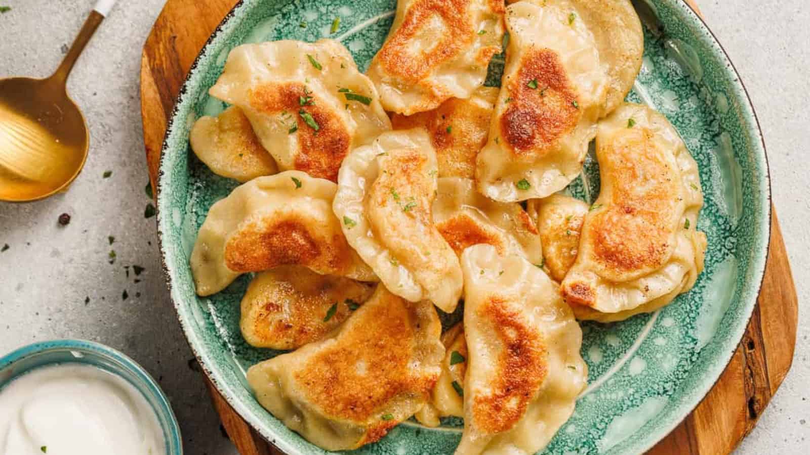 A green plate filled with golden-brown fried dumplings next to a bowl of white dipping sauce.