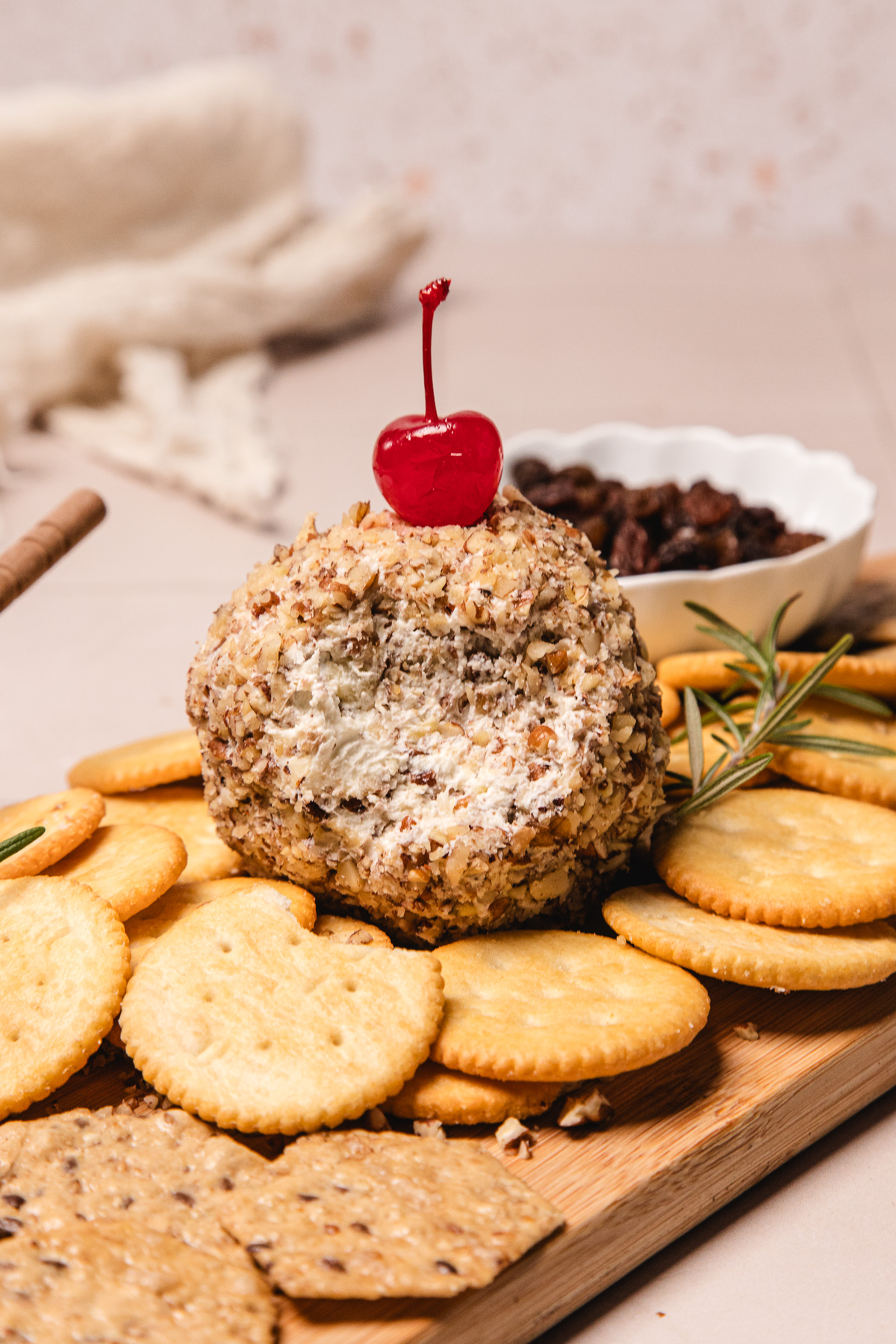 A pineapple cheese ball recipe topped with a cherry and coated in nuts, surrounded by crackers on a wooden board.