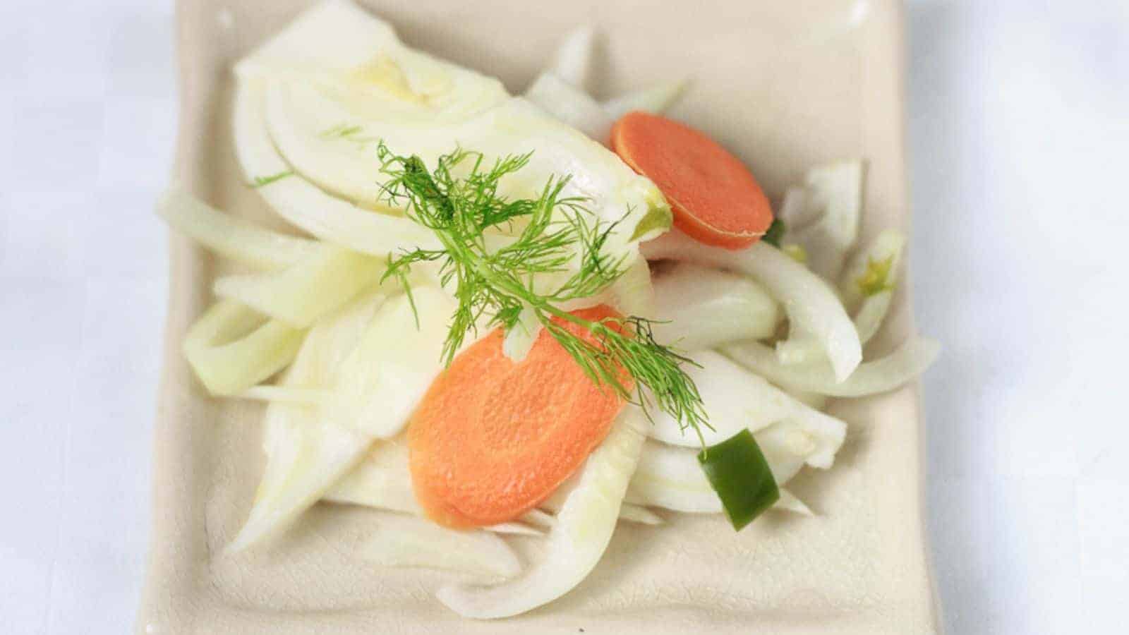 Sliced fennel, carrot, and green pepper on a beige plate, garnished with fennel fronds for a burst of fresh flavor.