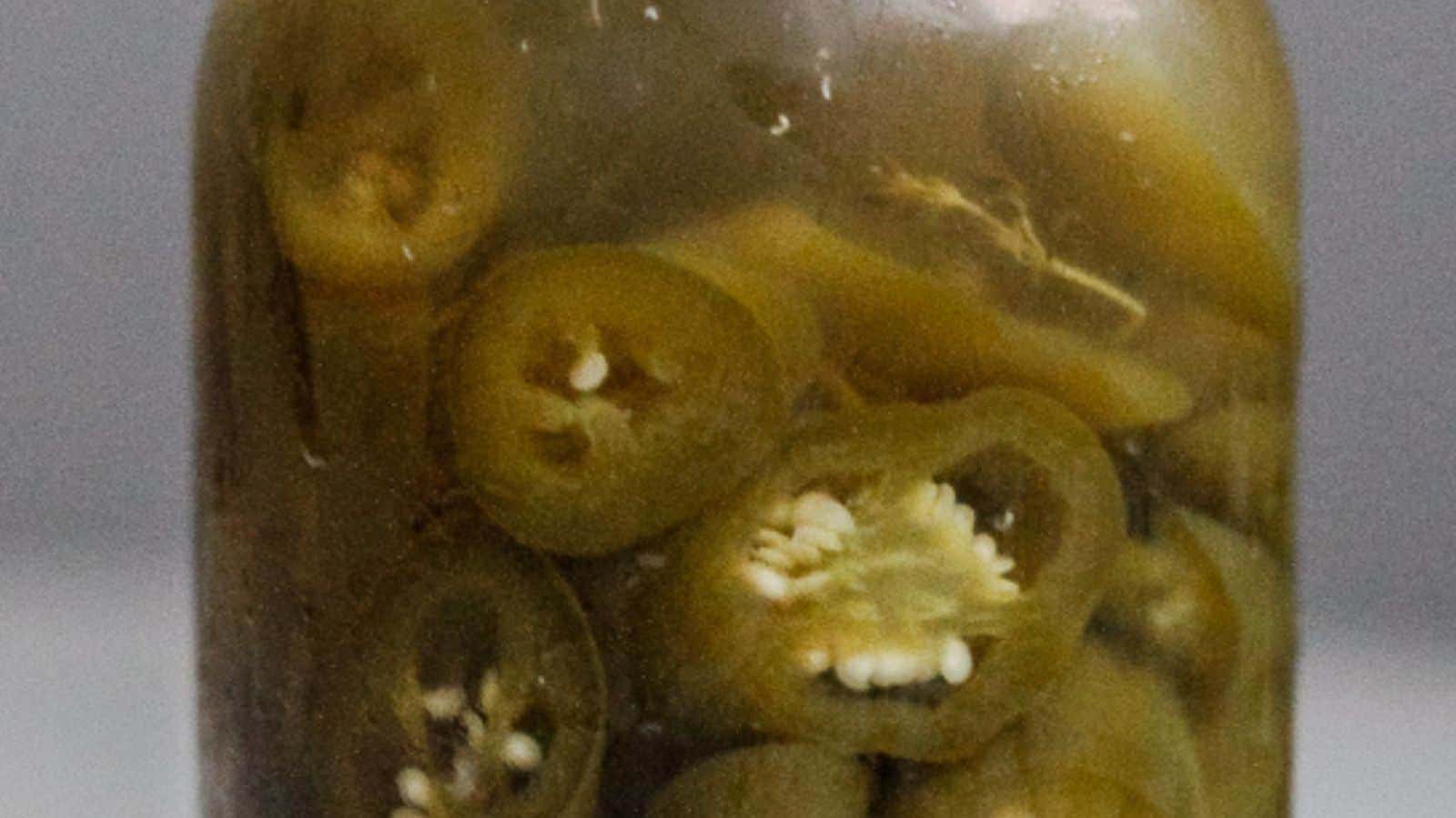 A glass jar filled with sliced pickled jalape&ntilde;os in brine&mdash;perfect for spicing up your easy afternoon recipes or serving as zesty picnic side dishes.