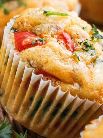Close-up of savory muffins with herbs, cheese, and vegetables in paper liners.