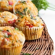 Four savory breakfast muffins with herbs, egg, and vegetables sit on a wicker tray, with fresh parsley in the background.
