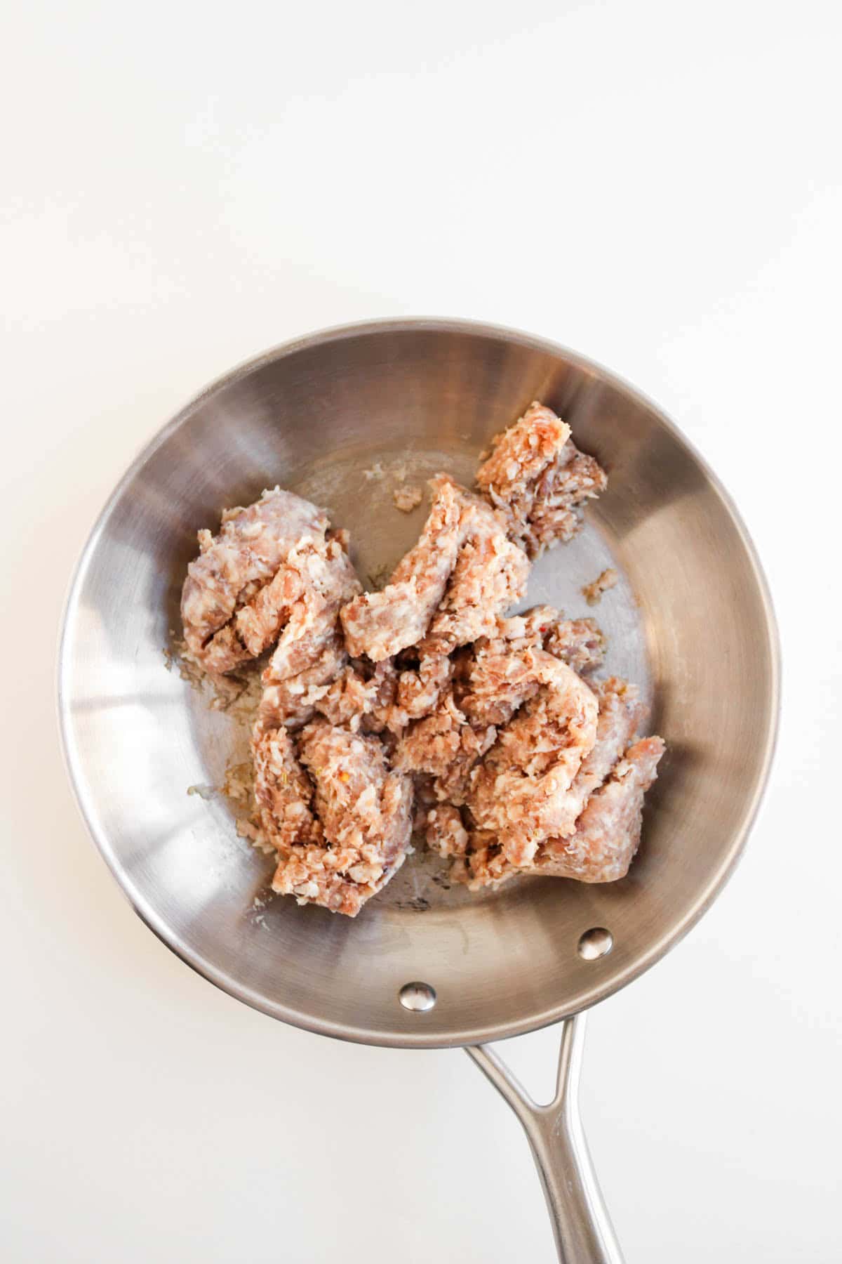 Raw ground meat and egg in a stainless steel frying pan on a white background.