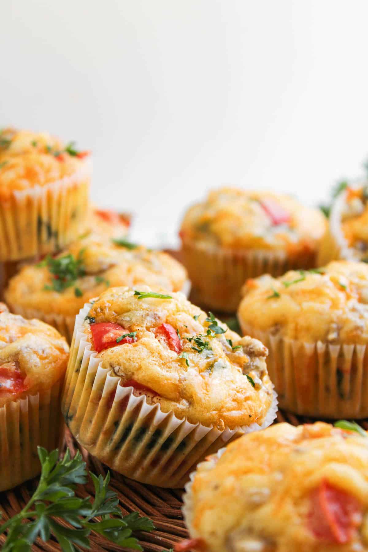 Egg, Sausage, Cheese Breakfast Muffins with visible herbs and vegetables in white paper liners, arranged closely together.
