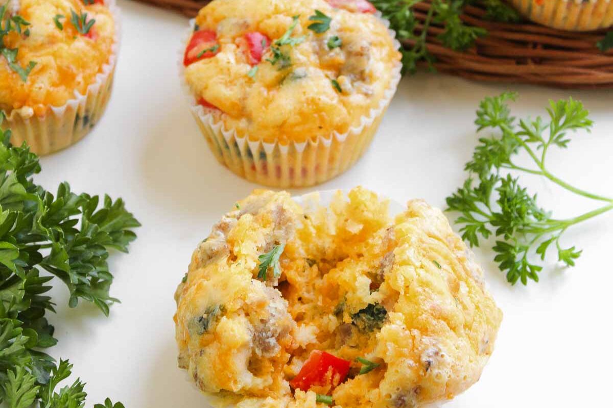 Cheese Breakfast Muffins with sausage, egg, and vegetables are garnished with fresh parsley and served on a white surface.