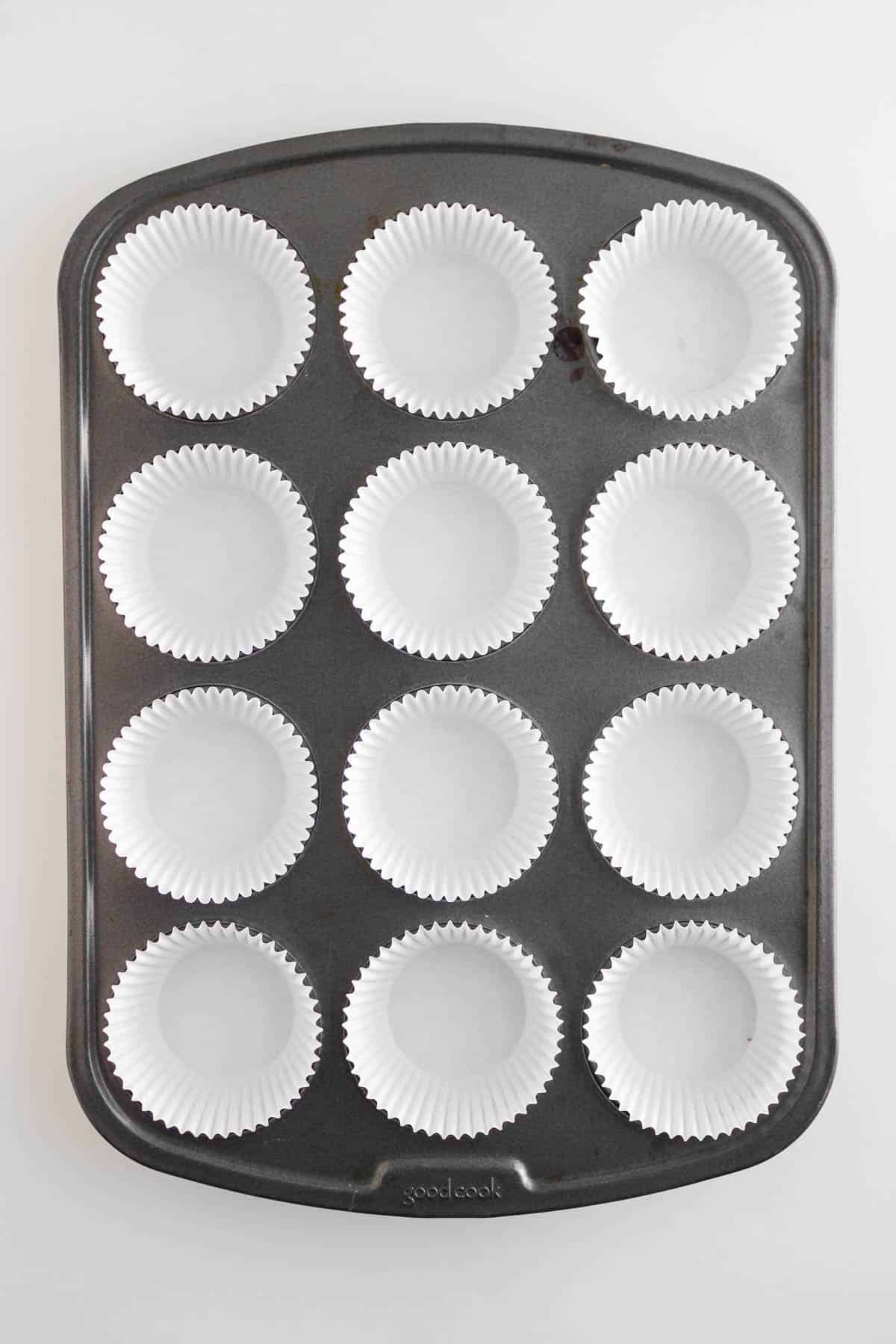 A muffin tin with 12 white paper cupcake liners arranged in each cup, perfect for baking breakfast muffins or savory egg and cheese muffins.