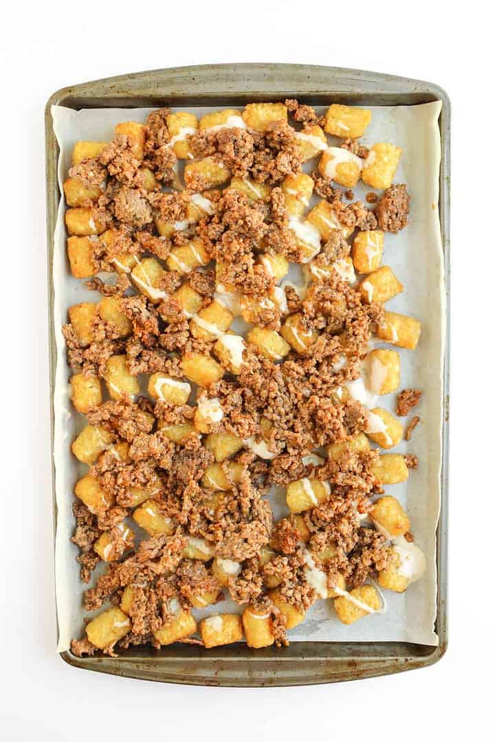 A sheet pan loaded with crispy tater tots, melted cheese, and savory ground beef creates irresistible tochos on parchment paper.
