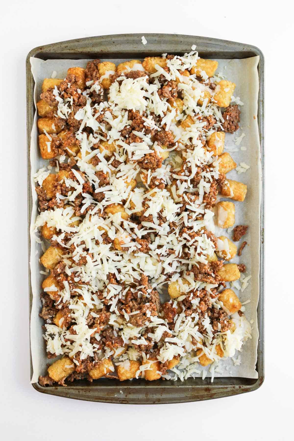A sheet pan lined with crispy tater tots, savory ground beef, and gooey cheese creates the perfect base for delicious sheet pan tochos, ready to be baked.