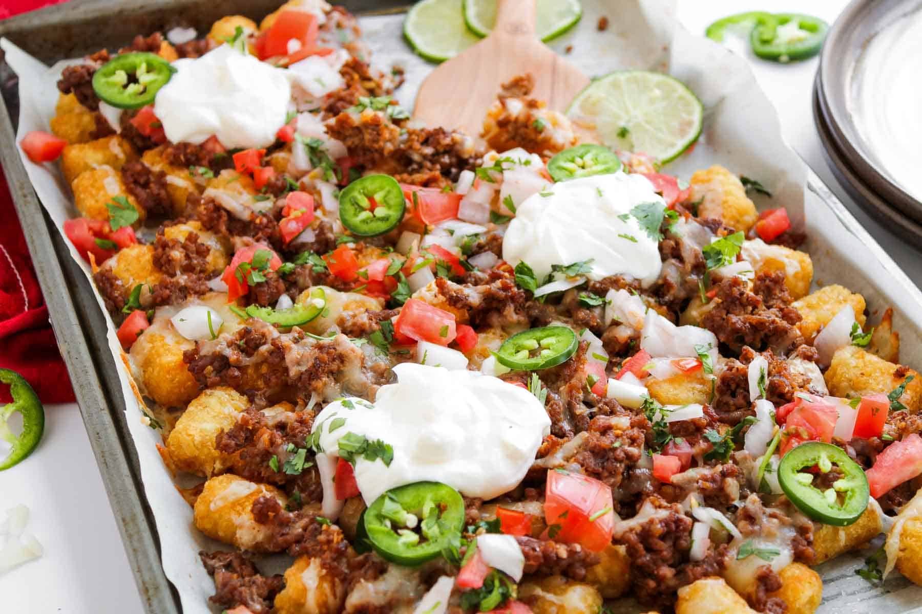 Sheet pan tochos topped with ground beef, tomatoes, jalape&ntilde;os, onions, cheese, cilantro, and sour cream.