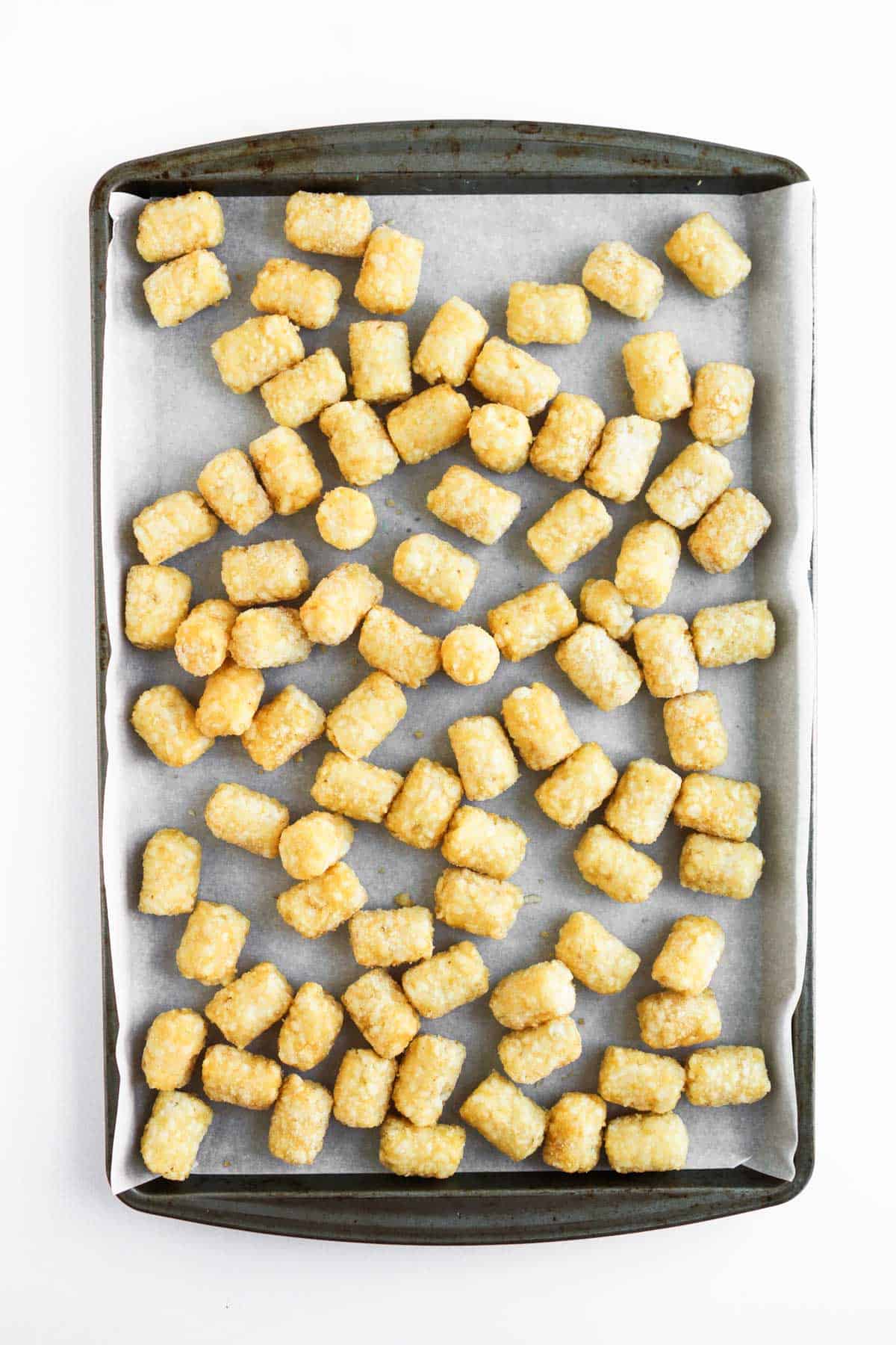Crispy frozen tater tots spread on a parchment-lined baking sheet, ready for baking&mdash;perfect for making tasty sheet pan tochos.