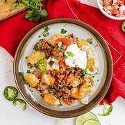 A plate of loaded totchos piled high with ground beef, sour cream, jalapeños, tomatoes, and fresh cilantro.
