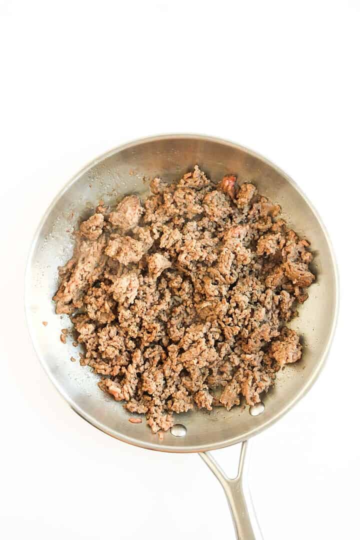 Cooked ground beef in a stainless steel skillet, perfect for making Tochos or adding to your favorite sheet pan recipes, viewed from above on a white background.